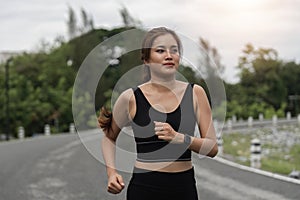Happy woman wearing sportswear jogging in the park. Young beautiful asian female in sports bra running outdoor. Workout