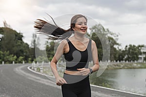 Happy woman wearing sportswear jogging in the park. Young beautiful asian female in sports bra running outdoor. Workout