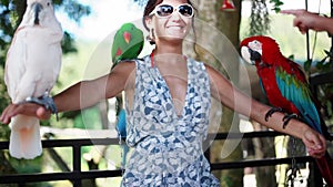 Happy woman wearing sunglasses holds parrots blue-gold Macaw parrot white parrot macaw in Koh Samui Paradise park