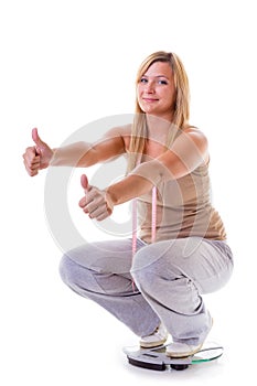 Happy woman wearing tracksuit squating on weighing machine