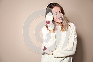 Happy woman wearing warm sweater and knitted mittens on beige background