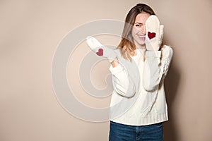 Happy woman wearing warm sweater and knitted mittens on beige background. Space for text