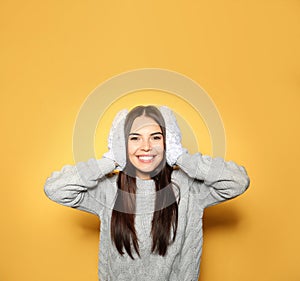 Happy woman wearing warm sweater and mittens on yellow background