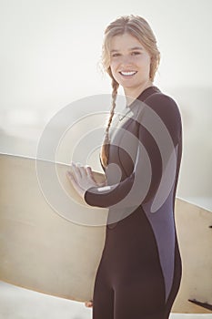 Happy woman in wetsuit holding a surfboard on the beach