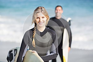 Happy woman in wetsuit holding a surfboard on the beach