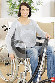 Happy woman on wheelchair using vacuum cleaner