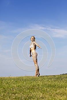 The happy woman in white bikini jumps in a summer green field against the blue sky