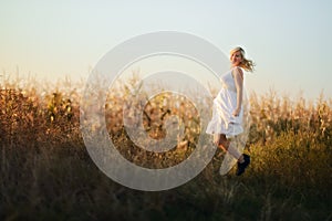 Happy woman in a white summer long dress jumping in front of the cornfield