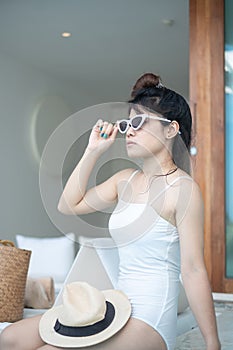 Happy woman in white swimsuit swimming in luxury pool hotel, young female with hat enjoy in tropical resort. Relaxing, summer