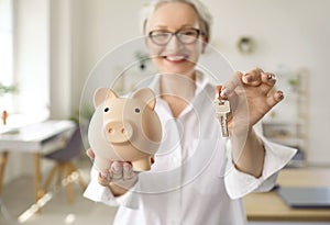 Happy woman who has saved money is holding a piggy bank and keys to her new house