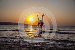 A happy woman who is jumping on the beach in sunrise on beautiful background with sea and sun shining on water