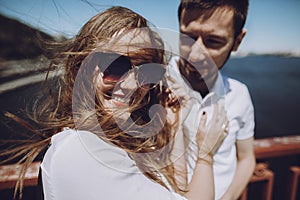 happy woman with windy hair in sunglasses smiling, stylish couple in love having fun on bridge in the summer city. modern woman