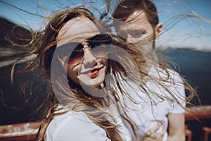 happy woman with windy hair in sunglasses smiling, stylish couple in love having fun on bridge in the summer city. modern woman