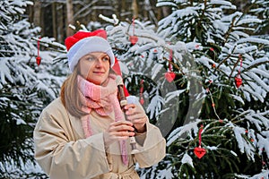 A happy woman in winter clothes plays the flute at the Christmas tree in a snow park on New Year Eve