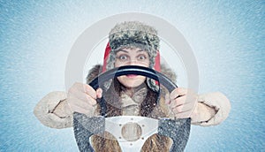 Happy Woman in winter clothes with a steering wheel, snow blizzard. Concept car driver.