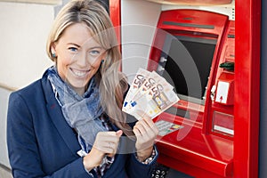 Happy woman withdrawing cash from ATM photo