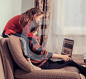 Happy woman working at home on computer and fun kid playing with mother. Sitting together on the sofa, hugging, smiling with