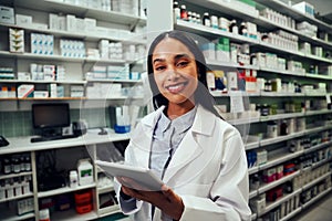 Happy woman working in pharmacy using digital tablet wearing labcoat looking at camera