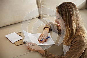 Happy woman writing letter on sofa at home