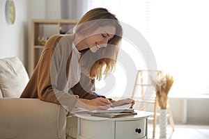 Happy woman writing letter at table in living room