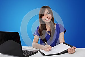 Happy woman writing on notebook, on blue background