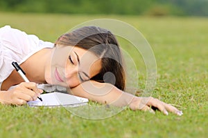 Happy woman writing on notebook lying on grass on a park