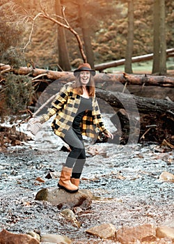 Happy woman in yellow shirt and hat walking along river in the autumn forest