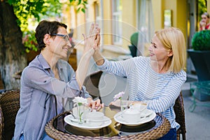 Happy women friends doing high-five and laughing in outdoor cafe in summer