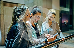 Happy women friends laughing while looking streaming video of social media app on mobile phone