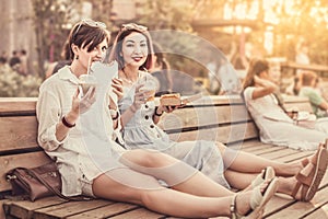 Happy women friends relax in park and eat street food to take away and drink soft drinks. Casual socializing and urban fast