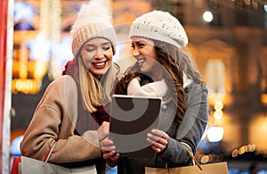 Happy women friends using digital tablet for online shopping at Christmas in the city.