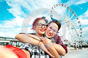 Happy women girlfriends taking selfie at ferris wheel on public area - Friendship and travel concept with pin-up styled girls