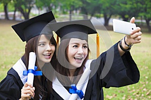 happy women in graduation gowns taking picture with cell pho