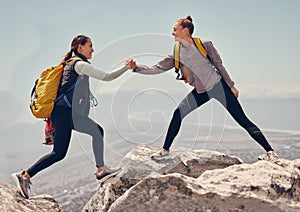 Happy women help while hiking up a rocky mountain in nature with backpack. Females friends exercise in nature park