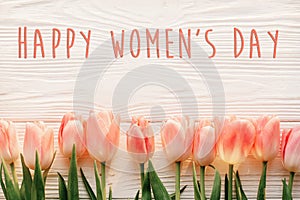 Happy women`s day text on pink tulips on white rustic wooden bac