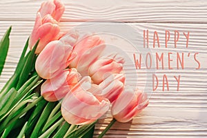 Happy women`s day text on pink tulips on white rustic wooden bac