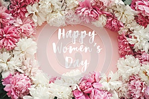 Happy Women`s Day text sign on stylish peonies flat lay. Pink and white peonies frame on pastel pink paper. Stylish floral