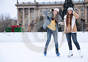 Happy women skating along ice rink outdoors. Space for text