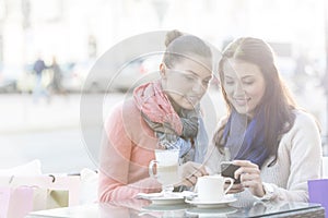 Happy women using cell phone at sidewalk cafe during winter