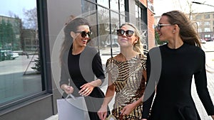 Happy women walk and talk on city street with shopping bags. slow-motion. Three Beautiful Young Women with Shopping Bags