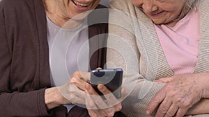 Happy women watching funny photos on smartphone and laughing, remembering past