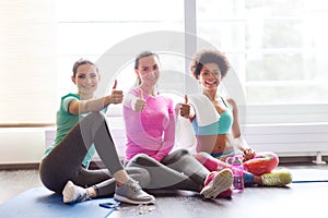 Happy women with water showing thumbs up in gym