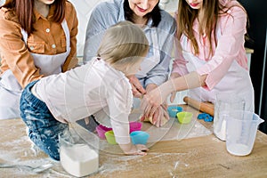 Happy women in white aprons baking together. Close-up photo of women hands and little baby preparing dough for baking