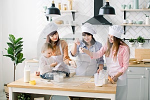 Happy women in white aprons baking together, Cutting out shapes from sugar cookie dough with cookie cutters. Little baby