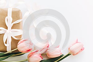 Happy womens day. Pink tulips and gift box with ribbon on white background, flat lay. Stylish tender image. Greeting card with