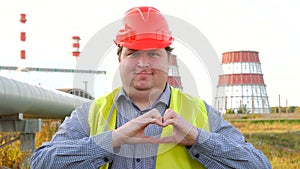 Happy worker, engineer, or electrician looking at the camera and showing love gesture in front of a power station