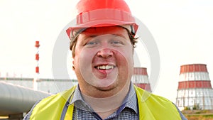 Happy worker, engineer, or electrician looking directly at the camera and winking in front of a power station