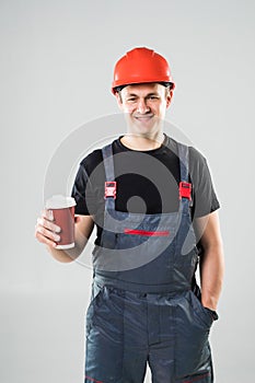 Happy worker in hard hat holding paper cup with coffee to go and smiling at camera isolated on white background