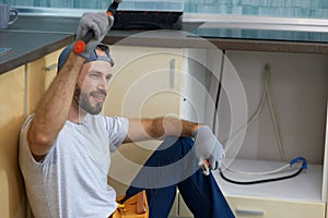 Happy worker. Portrait of cheerful young handyman holding a hammer and an adjustable wrench in his hands while sitting