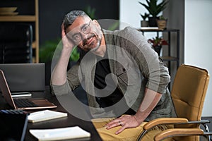 Happy worker sits in loft office, smiling with contentment work. Desk with computer, stationary, and other necessary